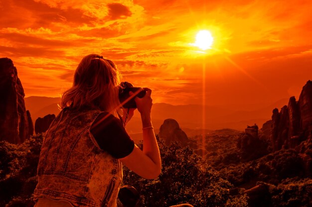 Photo woman photographing on retaining wall against mountains during sunset