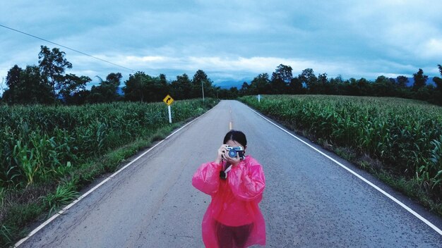 Woman photographing on road against sky