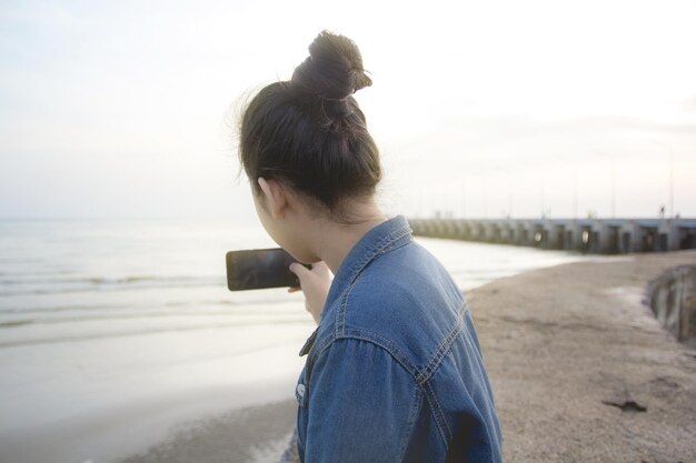 사진 해변 에서 휴대 전화 를 통해 바다 를 사진 을 찍는 여자