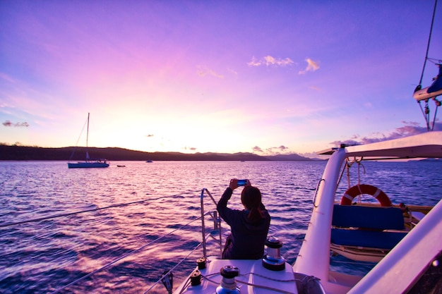 写真 夕暮れの船に座っている女性が海を撮影している