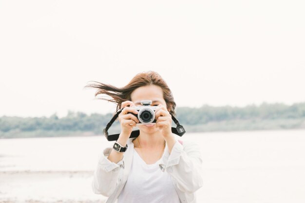 湖と澄んだ空に照らしてカメラを使って写真を撮っている女性