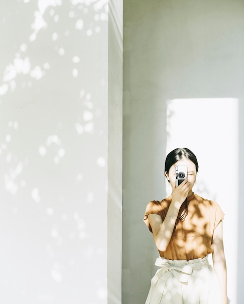 Woman photographing using camera against wall