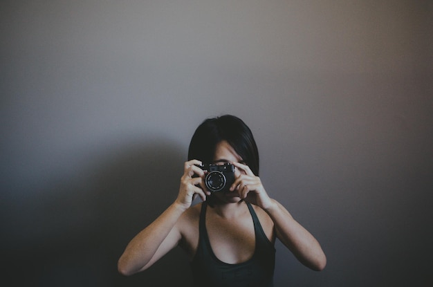 Woman photographing while standing against wall