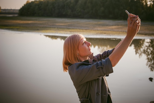 Photo woman photographing with mobile phone by lake