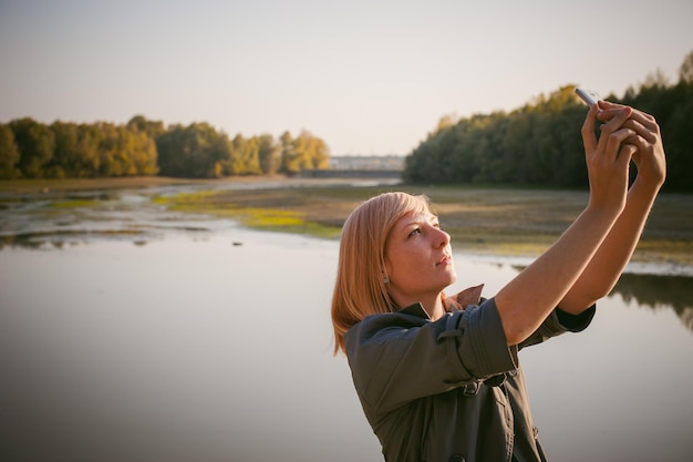 Foto donna che fotografia con il cellulare vicino al lago