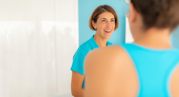 Женщина-физиотерапевт улыбается, оживленно беседуя с одним из своих пациентов в клинике.