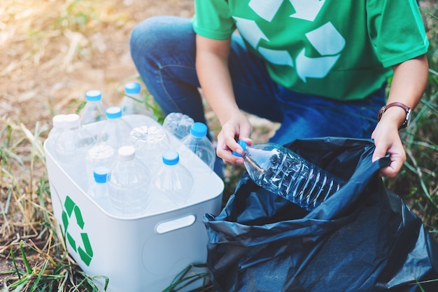リサイクルコンセプトのためにゴミ箱とビニール袋にゴミのペットボトルを拾う女性