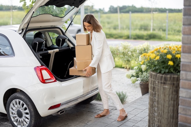 Woman picking up a parcels from a car trunk near a house