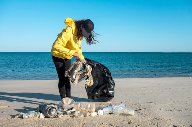 Woman picking up trash and plastics cleaning the beach with a
garbage bag. environmental volunteer activist against climate
change and the pollution of the oceans.