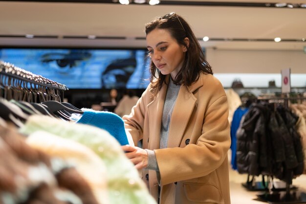 Woman picks out clothes at shopping mall dressed with thoughtful face