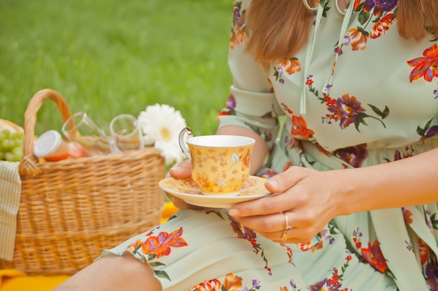 Woman on the picnic sits on the yellow cover and holds cup of tea or coffee. 