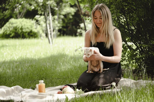 Woman on picnic with sphinx white cat on blanket in the garden