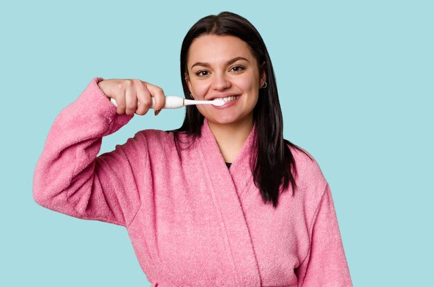 A woman in a pink bathrobe holds an electric toothbrush ready for a fresh and clean smile