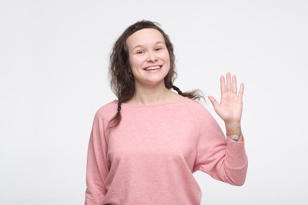 Woman in pink clothes waving hand saying hello greeting her friends