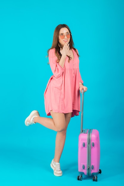 A woman in a pink dress holds in her hands a big pink suitcase luggage trip
