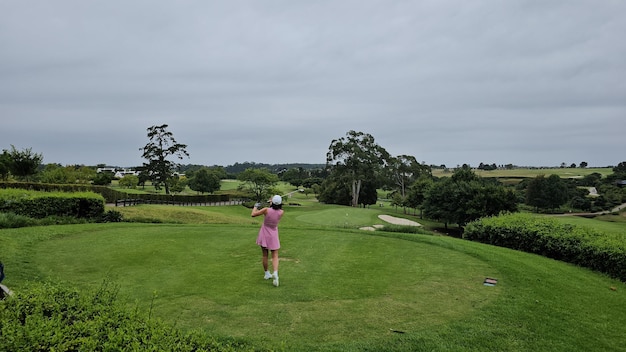 분홍색 드레스 를 입은 여자 가 골프 를 하고 있다