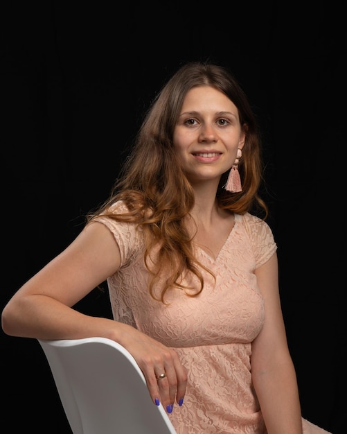 A woman in a pink dress stands in front of a black backdrop