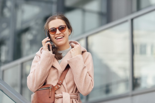 Donna in abito rosa che parla con smarthone all'aperto su sfondo grigio urbano della città