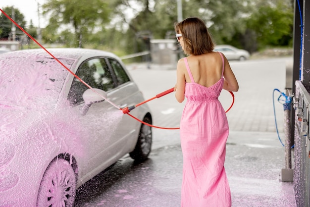 Woman in pink dress washing her tiny car with nano foam at car wash