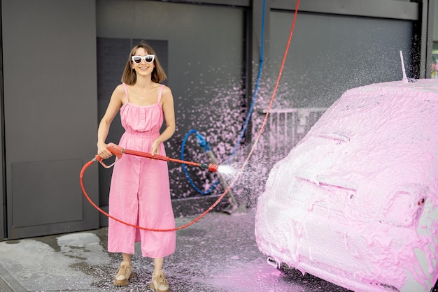 Woman in pink dress washing her tiny car with nano foam at car wash