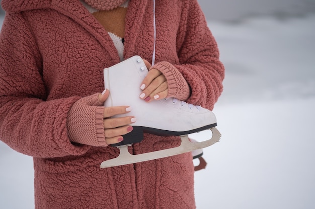 woman in a pink eco fur coat holds white skates on her shoulder