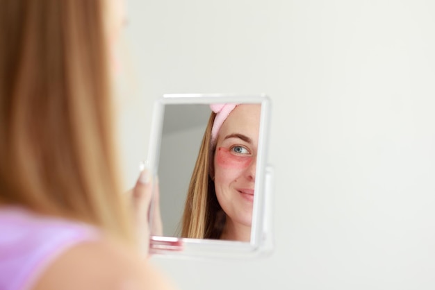 Woman in pink patches looks in the mirror on a white background