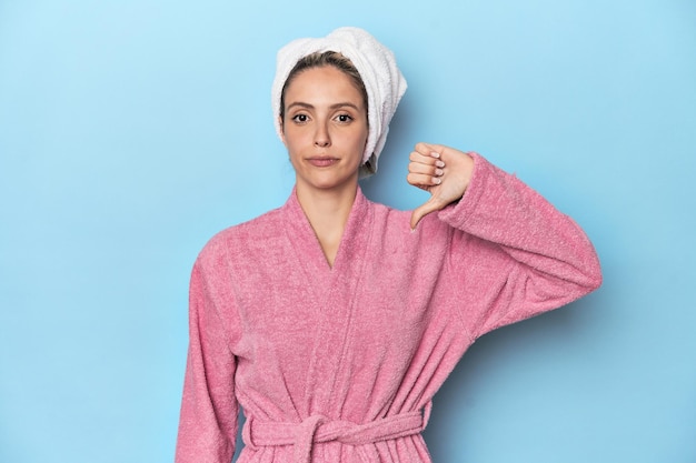 Woman in pink robe after shower showing a dislike gesture thumbs down Disagreement concept