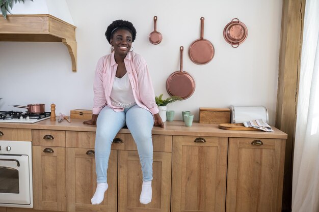 Una donna in camicia rosa seduta sul tavolo in cucina