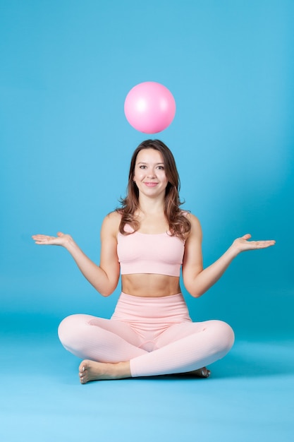 woman in pink sportswear sits crosslegged and throws a ball