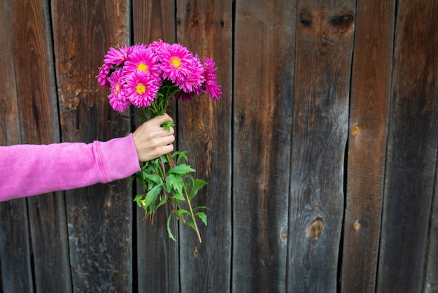 A woman in a pink sweater holds a beautiful pink bouquet of flowers in her hands against the background of a wooden wall. place for an inscription