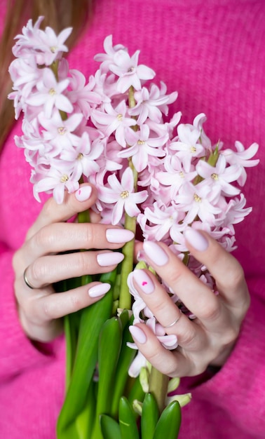 A woman in a pink sweater holds a blooming pink hyacinth in her hands