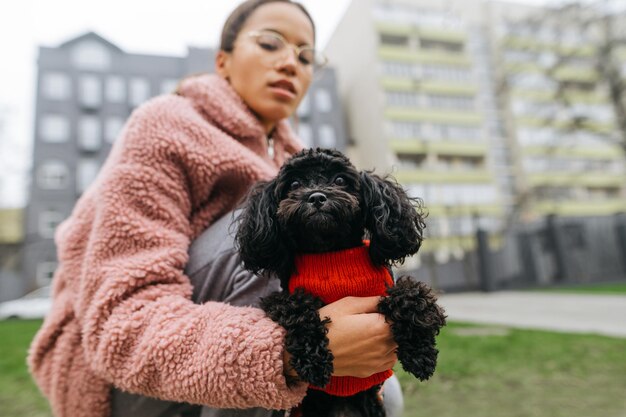 ピンクのセーターの女性は、ウォークドッグのクローズアップでトイプードルを楽しんでいます