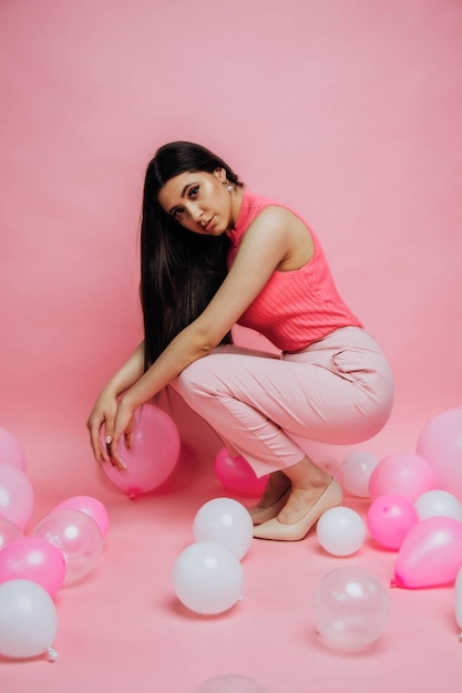 A woman in a pink tank top sits on pink balloons.