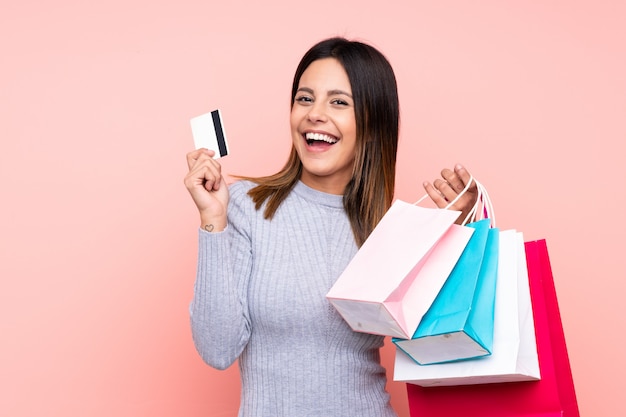 Woman over pink wall holding shopping bags and a credit card