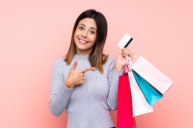 Woman over pink wall holding shopping bags and a credit card