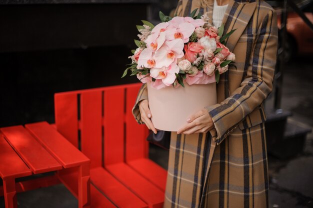 花のピンクの箱を持って格子縞の秋のコートを着た女性