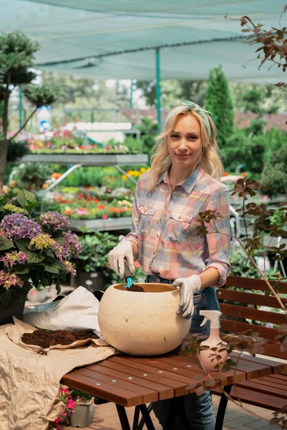 Woman planting flower in pot using dirt in garden center