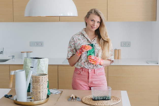 Photo woman planting seeds in boxes in beautiful interior. spring planting sprinkles the ground with home garden tool.