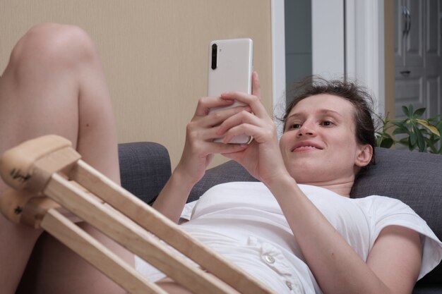 Woman in a plaster cast lies on the couch at home and using\
smart phone.