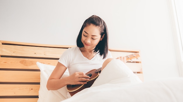 Woman play ukulele on her bed in the morning.