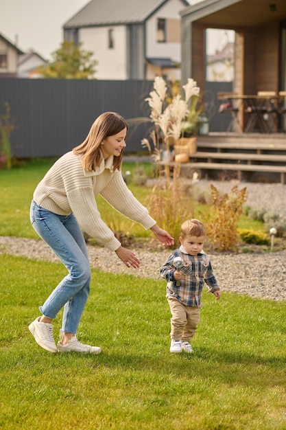 Woman playing catching child on green lawn near house