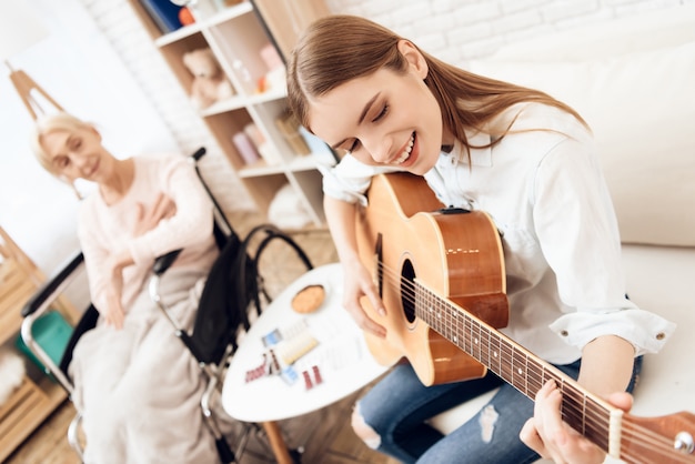 Foto donna che suona la chitarra per la vecchia signora in sedia a rotelle.