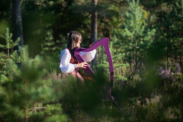 숲 속 의 나무 들 에 대항 하여 하프 를 연주 하는 여자