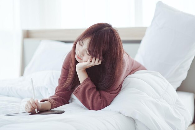 흰색 침실의 침대에서 태블릿을 하고 있는 여성