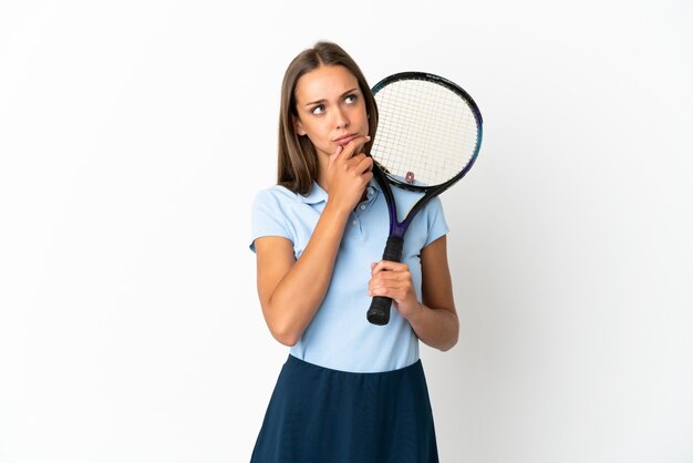 Woman playing tennis over isolated white wall having doubts