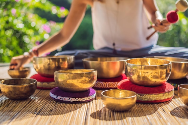 Foto donna che gioca su una ciotola tibetana mentre è seduto su una stuoia di yoga contro una cascata tonnellata d'epoca bella ragazza con perline di mala meditando