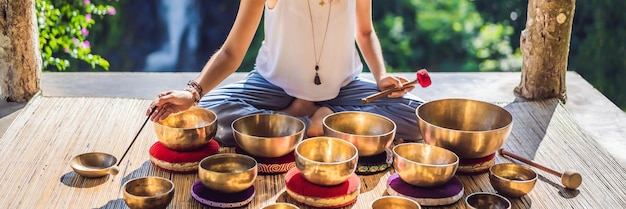 Woman playing on tibetan singing bowl while sitting on yoga mat against a waterfall vintage tonned