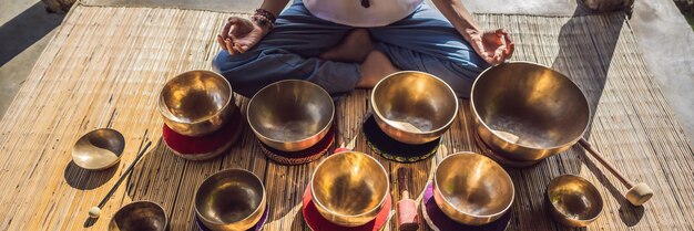 Photo woman playing on tibetan singing bowl while sitting on yoga mat against a waterfall vintage tonned