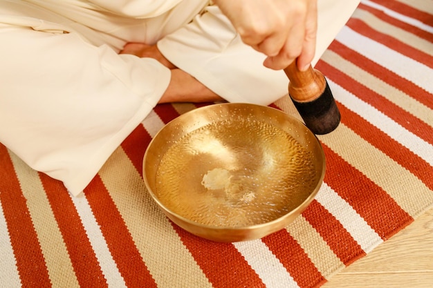 Woman playing on a tibetian singing bowl in cozy room meditating in a yoga