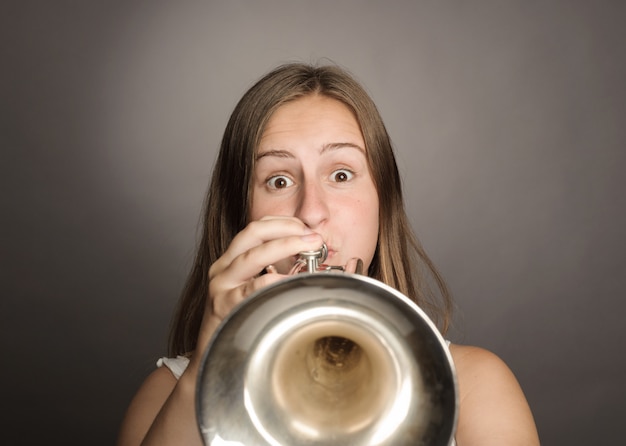 Woman playing trumpet on gray